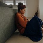 young woman sitting on floor holding her hands against her body